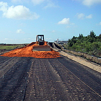 Una excavadora esparce arena sobre una geomalla Basetrac Grid colocada como refuerzo de la capa de base en una obra.