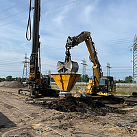 Excavadora llena una columna revestida de Ringtrac® con ayuda de una tolva