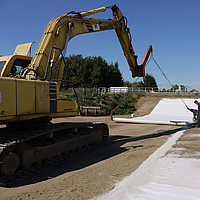 Excavadora utiliza un travesaño de colocación para extender las esteras de bentonita Tektoseal® Clay