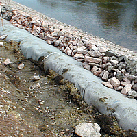 Geotextil no tejido y piedras al borde del agua para proteger las orillas