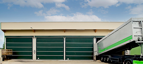 Lubratec Stabitore Tres Lubratec Stabitore verdes cerrados en un almacén beige. Un camión está siendo descargado en la puerta abierta a la derecha.