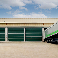 Cuatro puertas verdes en un pasillo. Un camión con material termina en una de las puertas