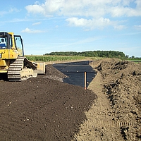 Una excavadora esparce tierra sobre una rejilla Basetrac ya colocada en la obra.