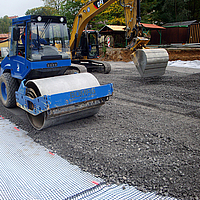 Un rodillo compacta grava y piedra triturada sobre el geocompuesto Basetrac® Duo-C